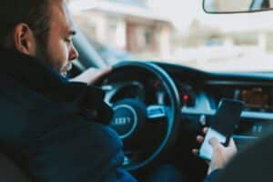 A driver sitting behind the wheel of a car looking down at a mobile phone instead of the road.